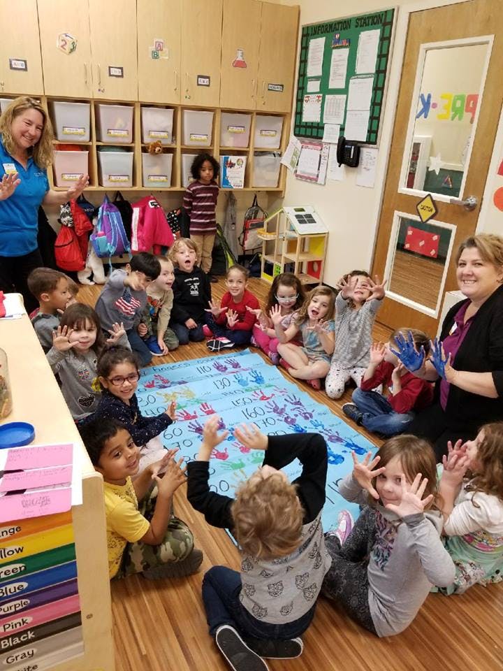 Two adults and multiple children sitting on the floor in a classroom