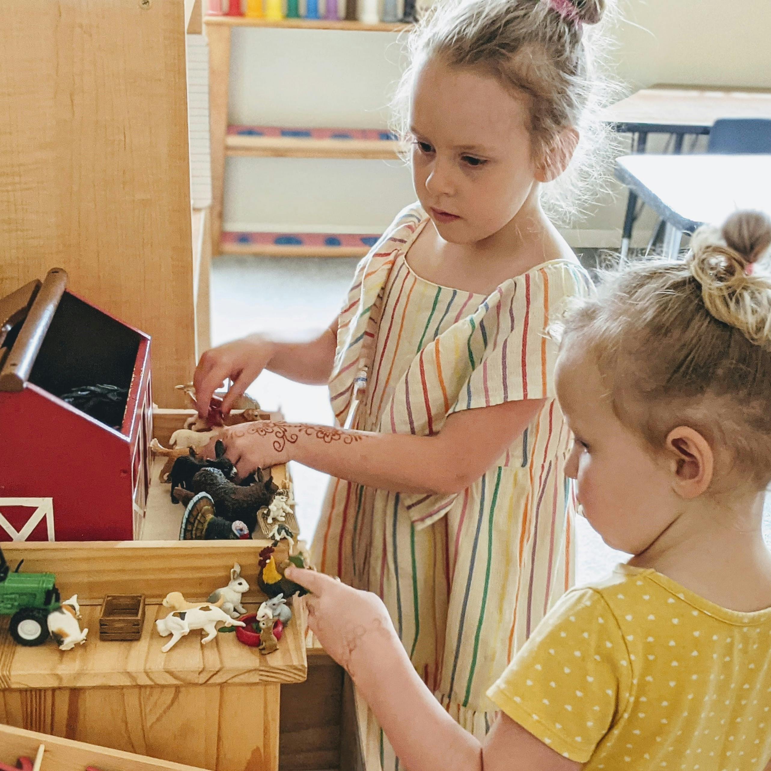 Two children playing with farm animal toys and a red barn
