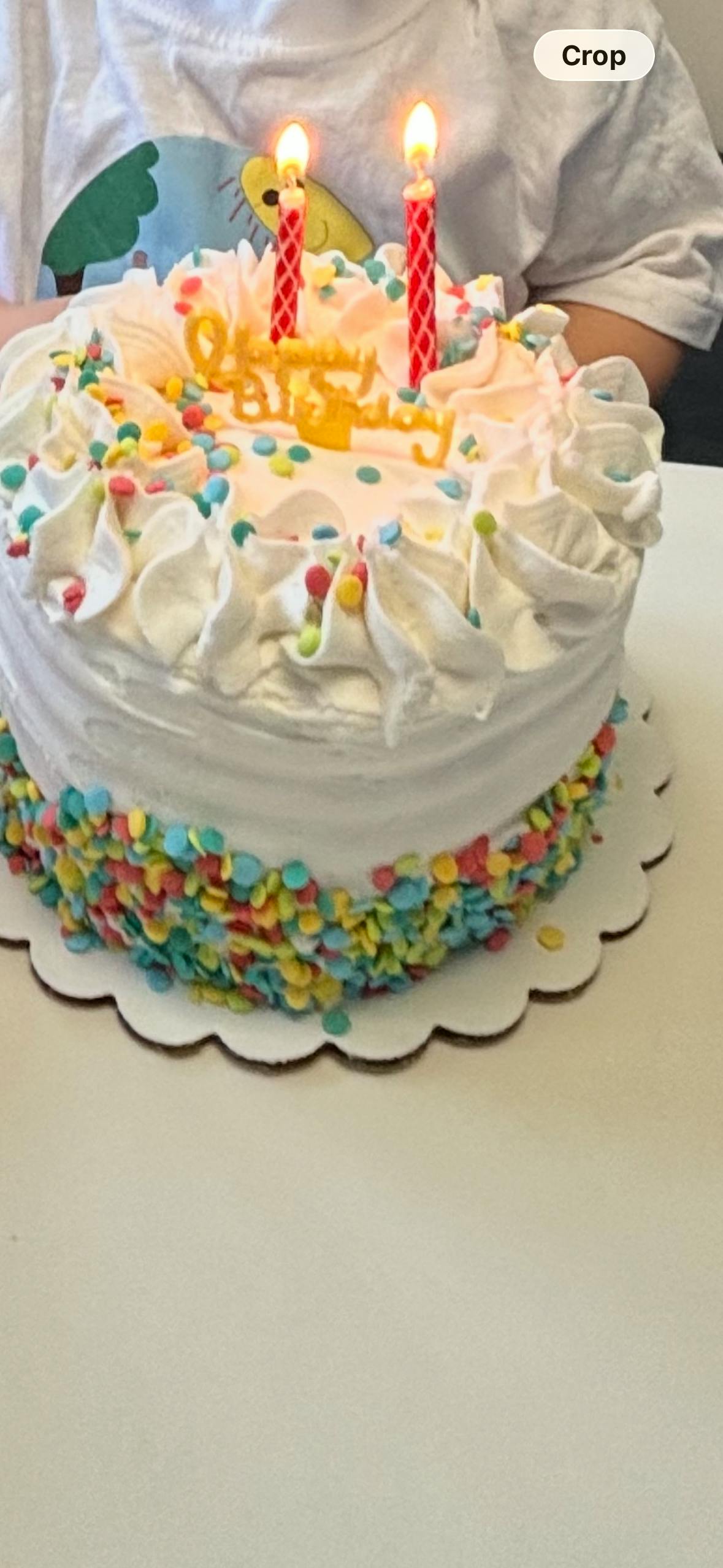 Birthday cake with frosting, colorful sprinkles, and two lit candles