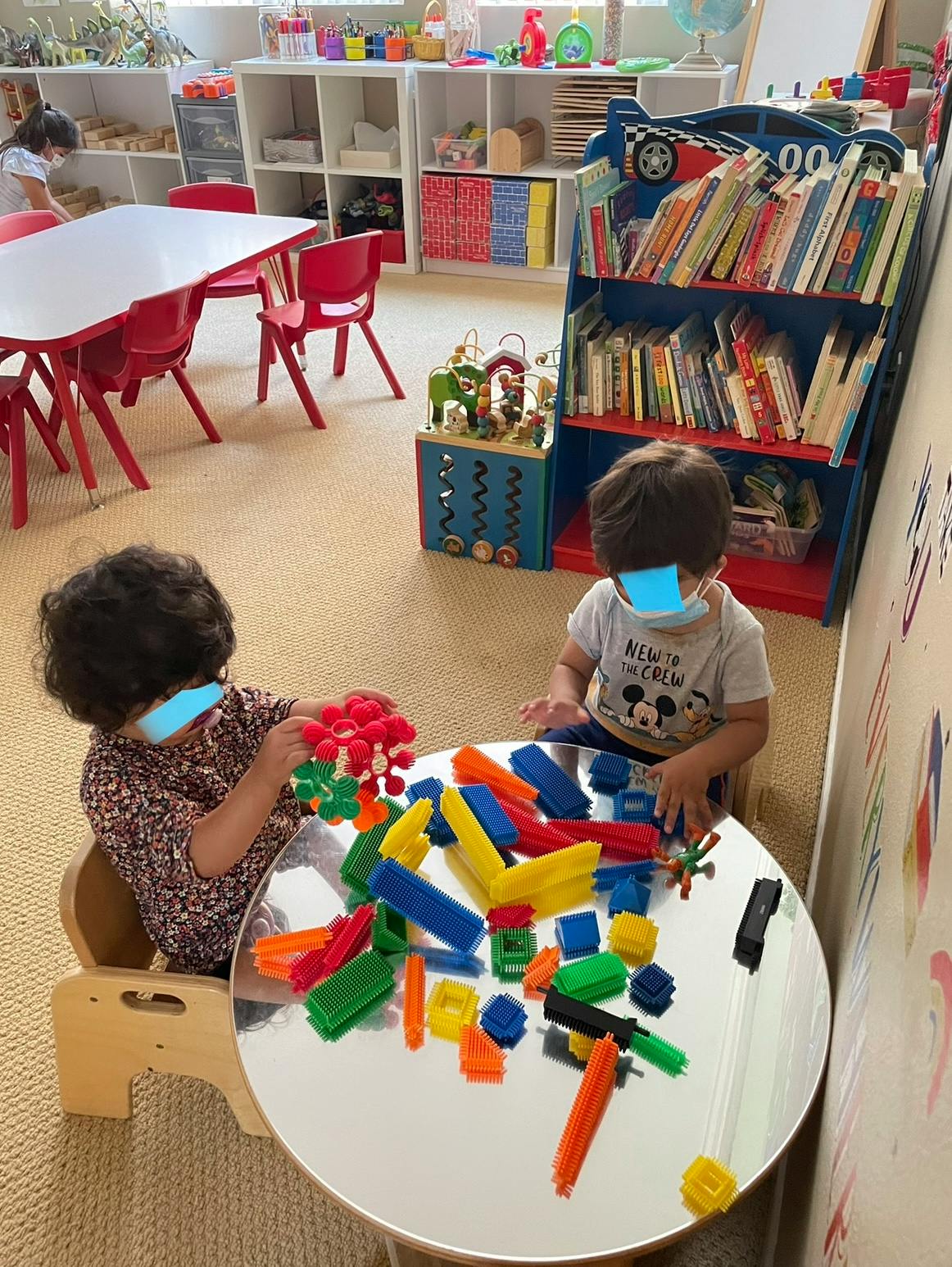 Two children playing with colorful building blocks at a table in a classroom