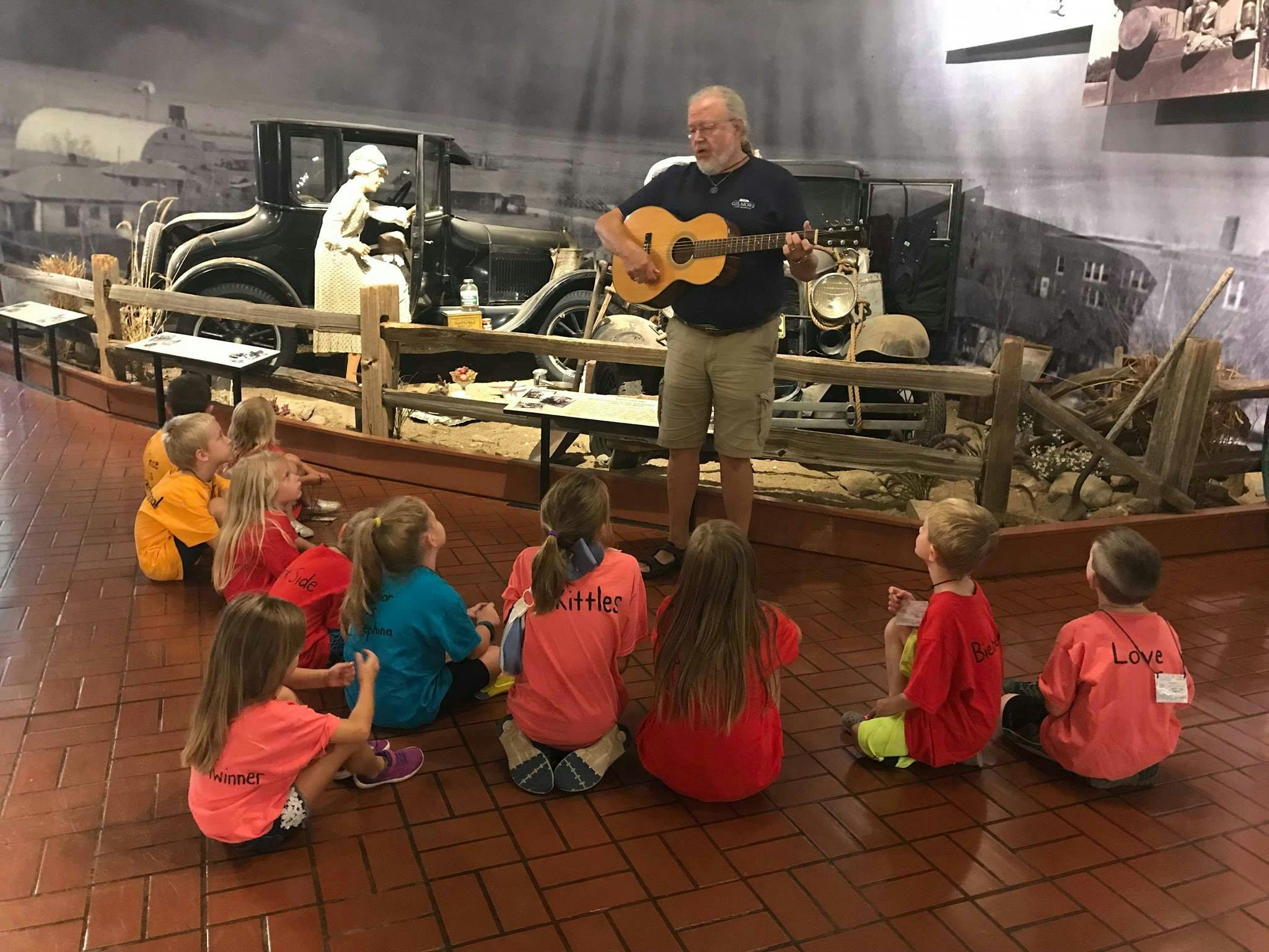 Person playing guitar for a group of children sitting on the floor