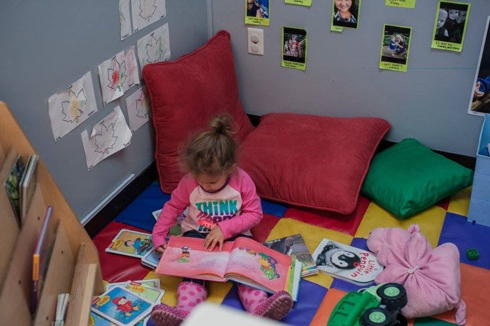 Child sitting on floor reading a book in a classroom corner