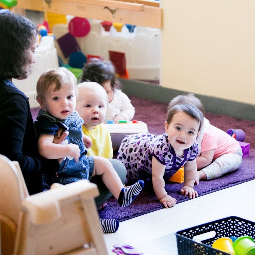 Person holding a child, with other children playing on the floor
