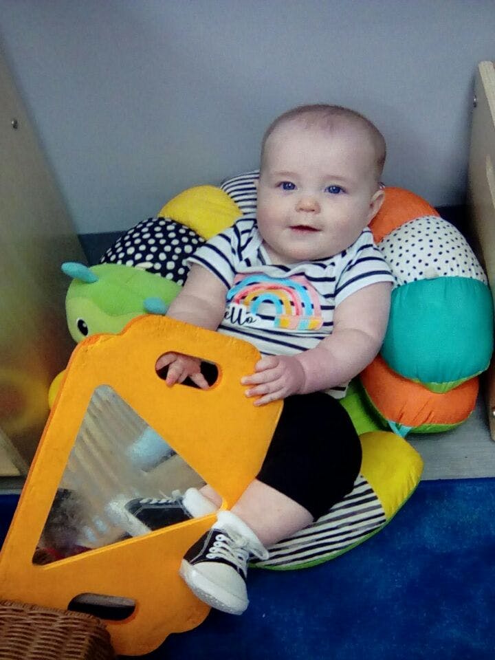 Child sitting on a colorful caterpillar toy, holding a yellow mirror toy