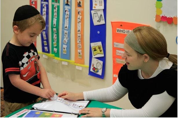 Child and person looking at papers on a table in a classroom