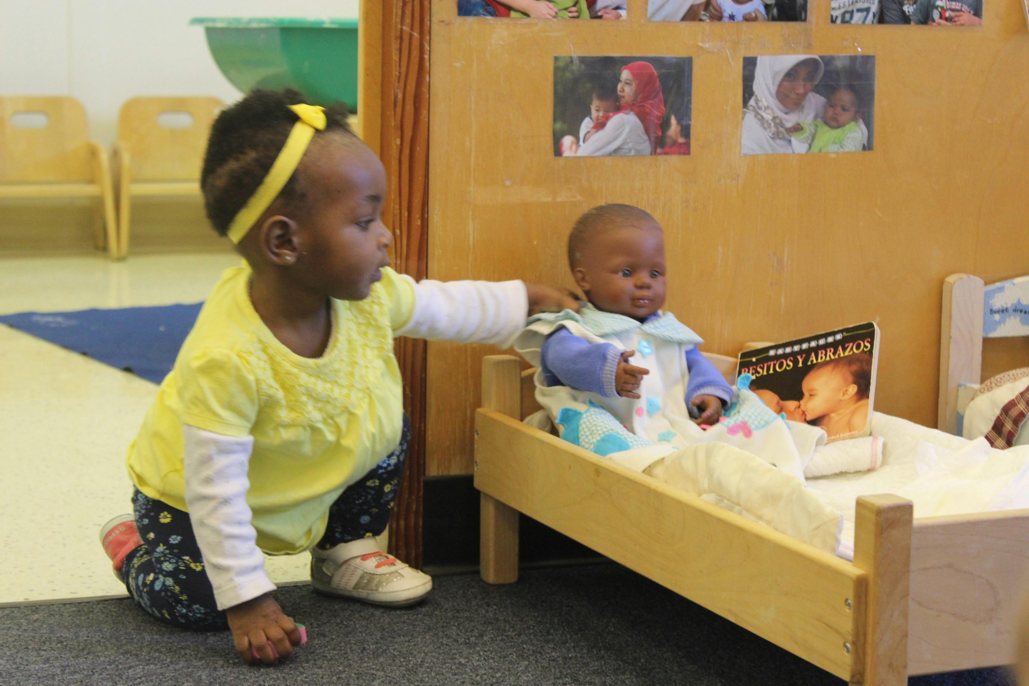 Child reaching out to a doll in a small bed