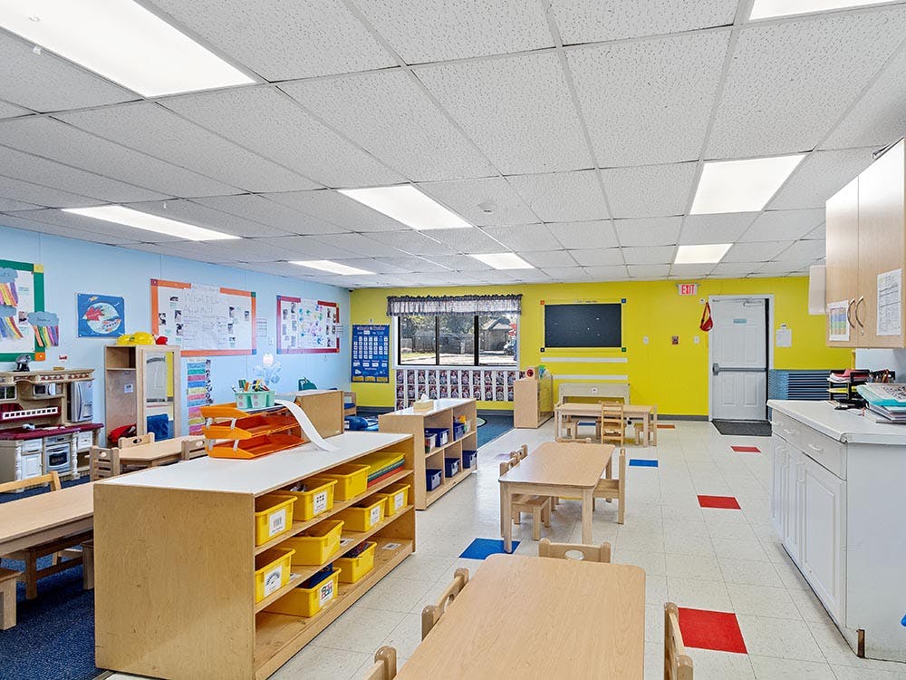 Empty classroom with small tables, chairs, and shelves with colorful bins