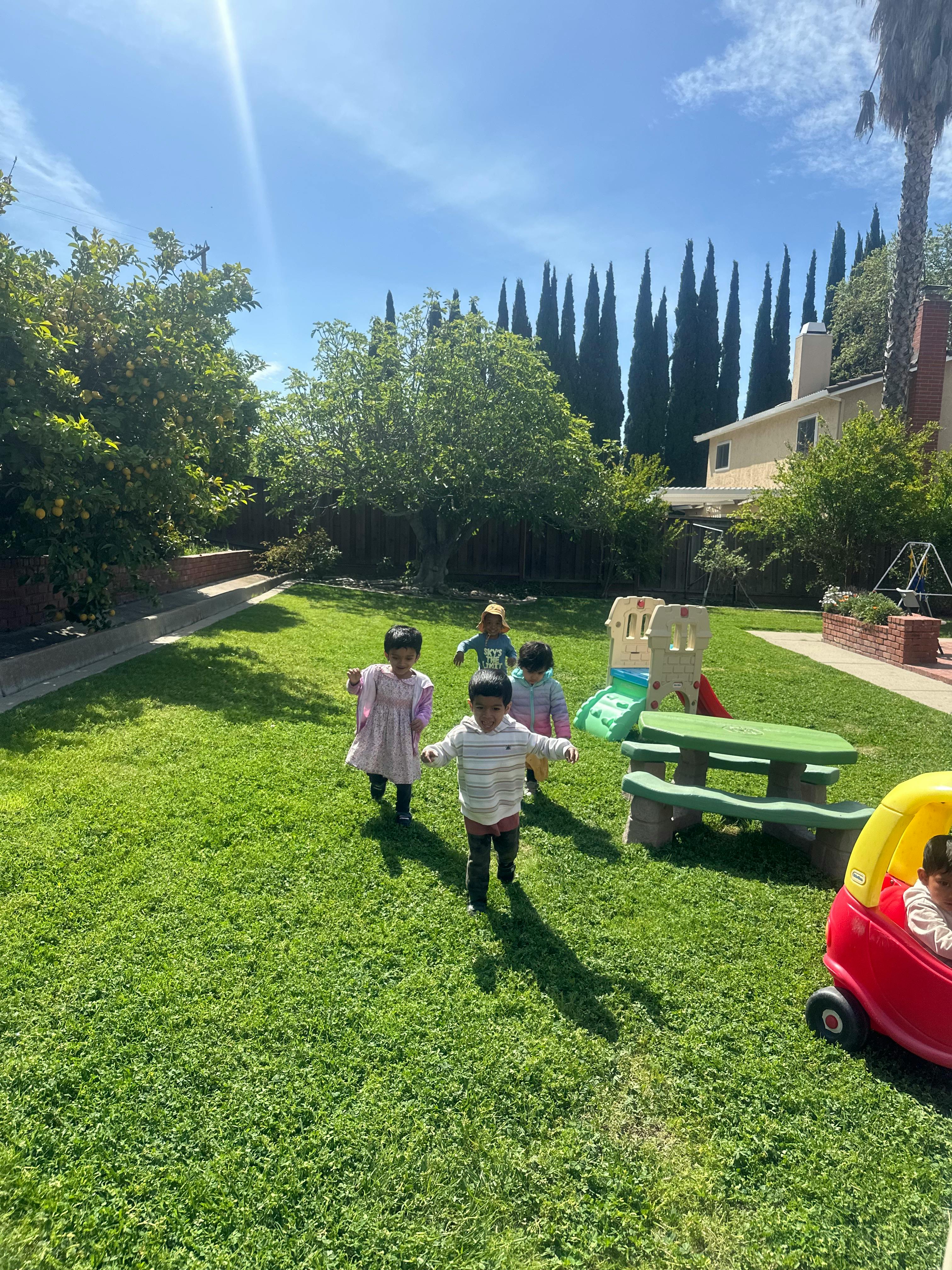 Children playing in a grassy backyard with a picnic table and toy car