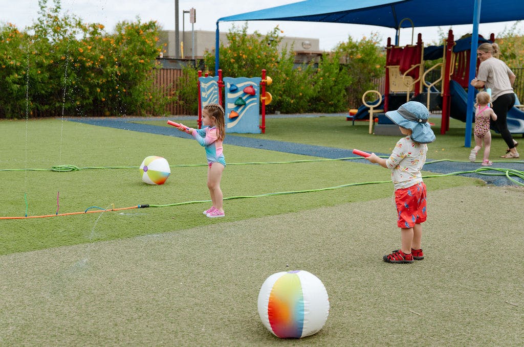 Children playing with water toys on a playground with beach balls