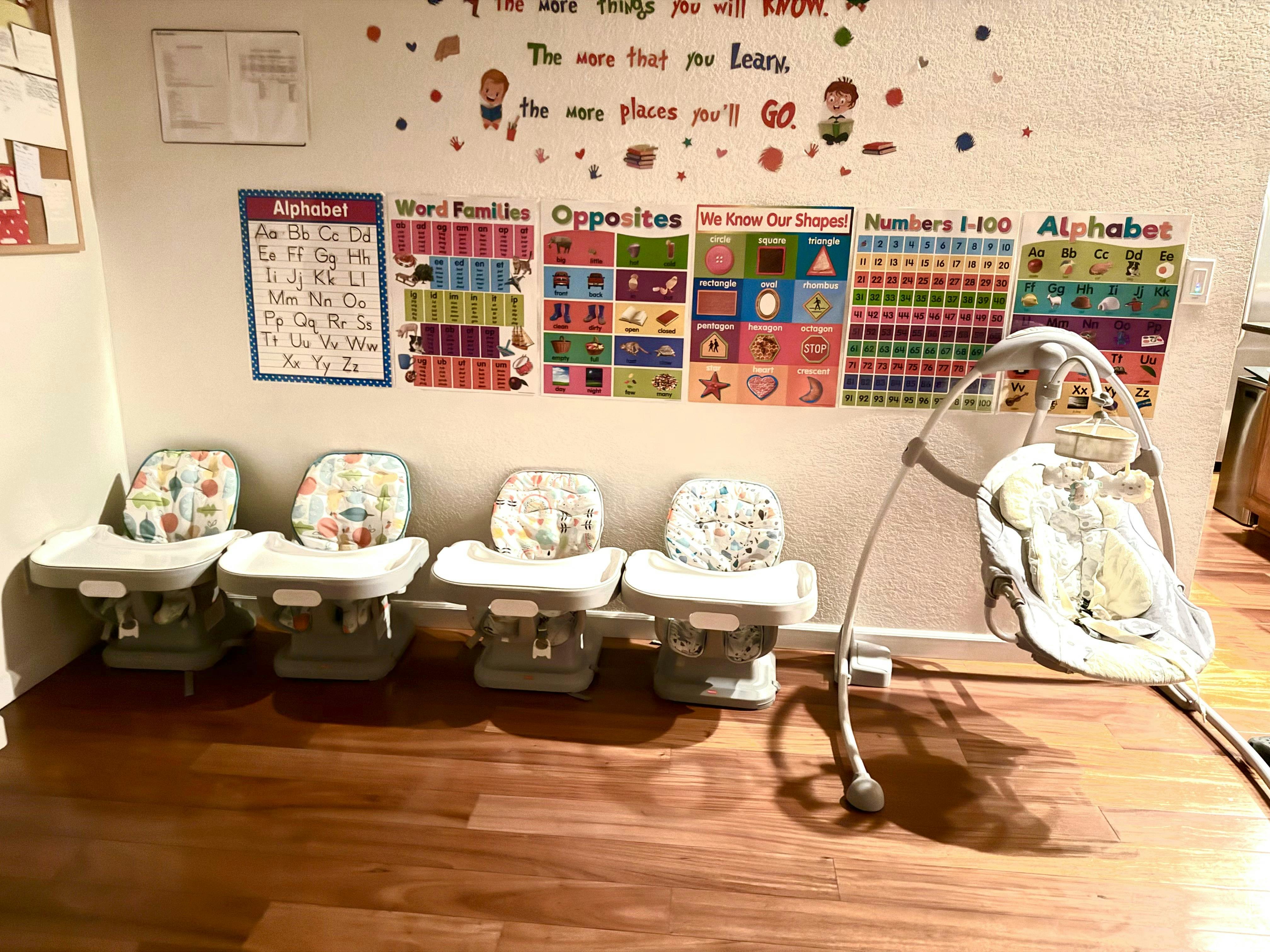 Four high chairs and a baby swing in front of a wall with educational posters