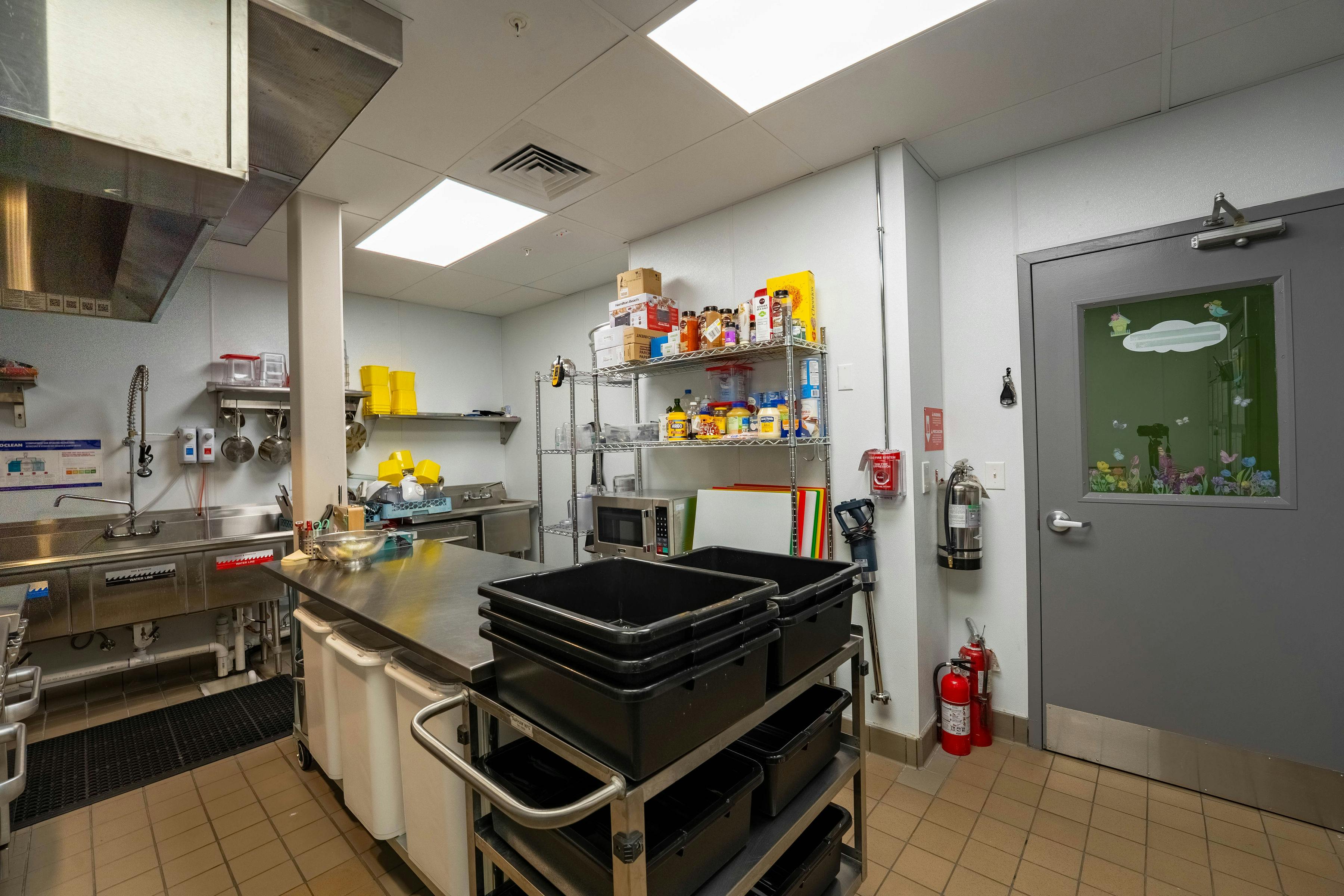 A commercial kitchen with stainless steel counters, sinks, and storage shelves