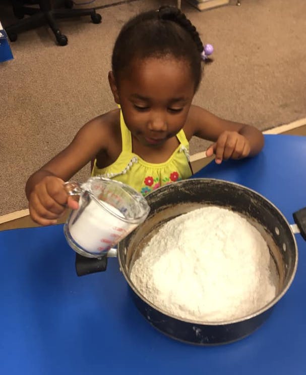 Child pouring from a measuring cup into a pot of flour