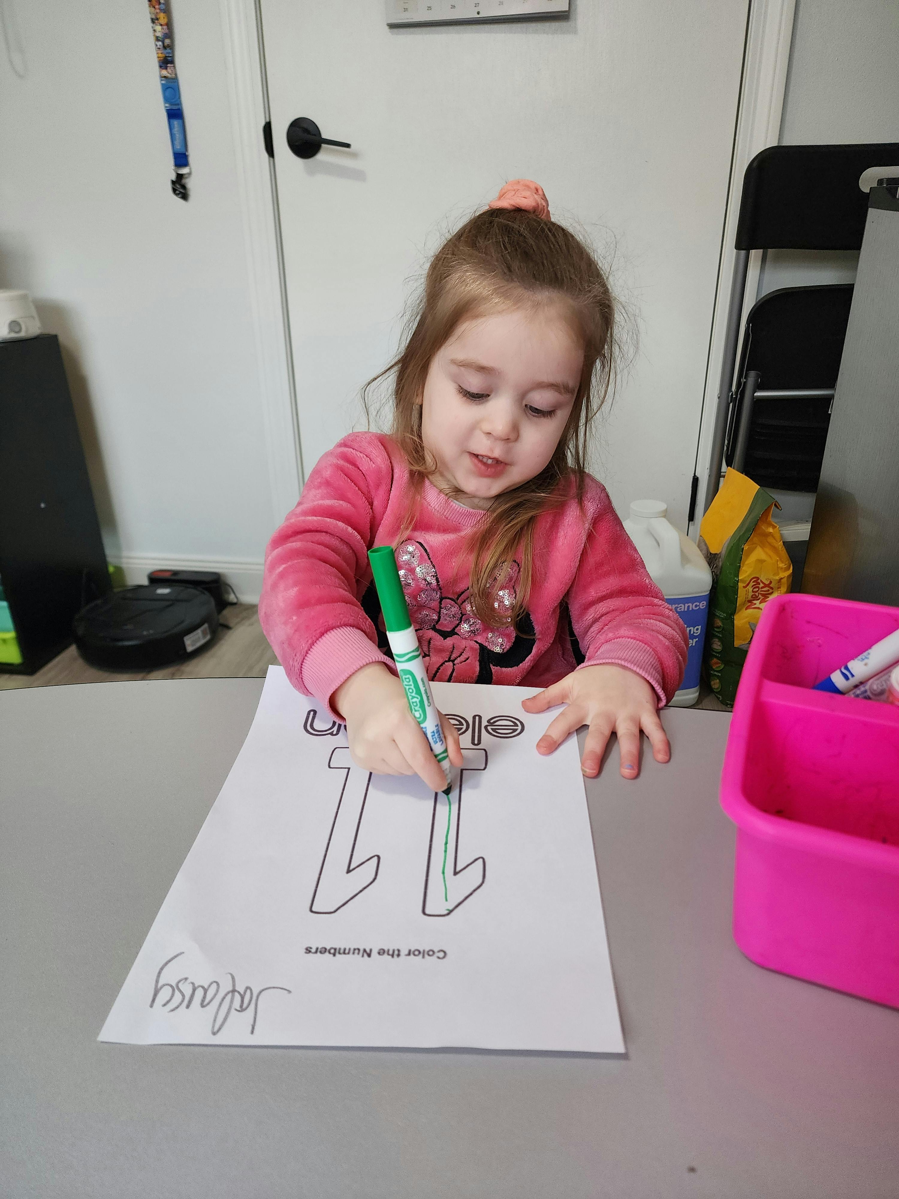 Child coloring a number 11 on a paper with a green marker