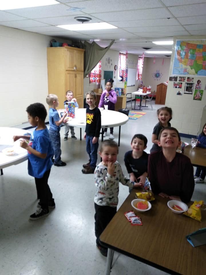 Children standing around tables in a classroom