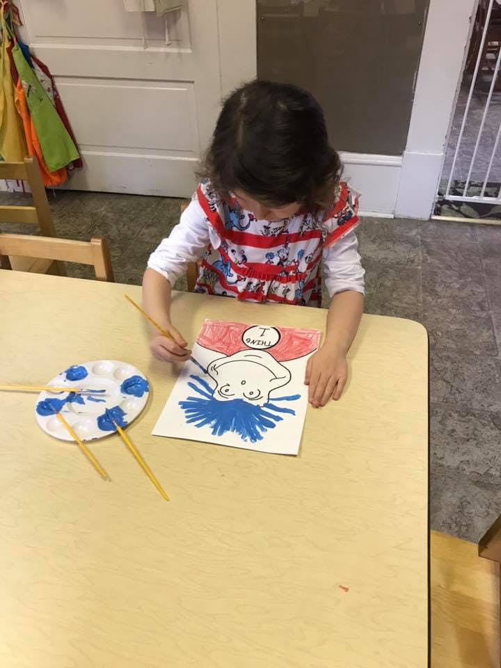 Child painting a drawing of a character with blue hair at a table