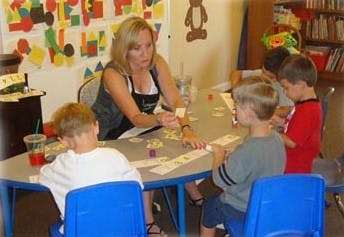 Adult and children playing a game at a table in a classroom