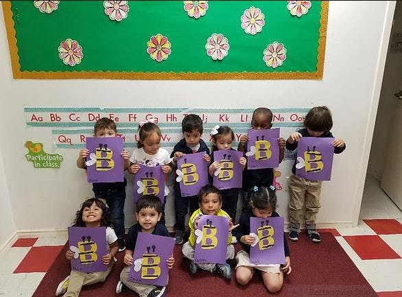 Group of children holding up purple papers with the letter B and a bee