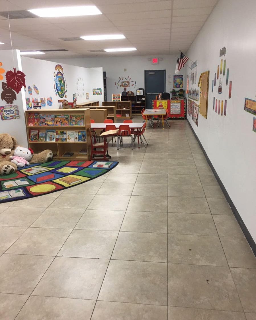 Empty classroom with small tables and chairs, bookshelves, and a colorful rug