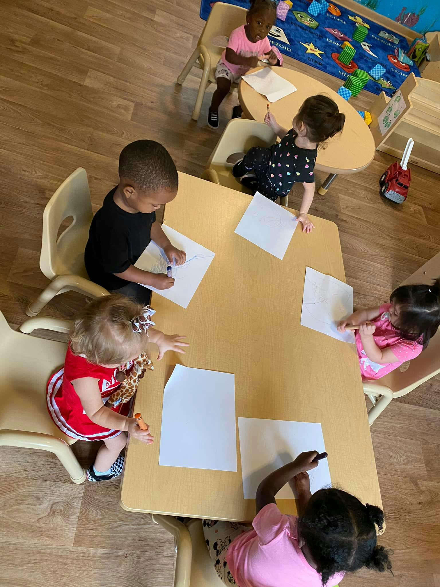 Children sitting at tables drawing on paper