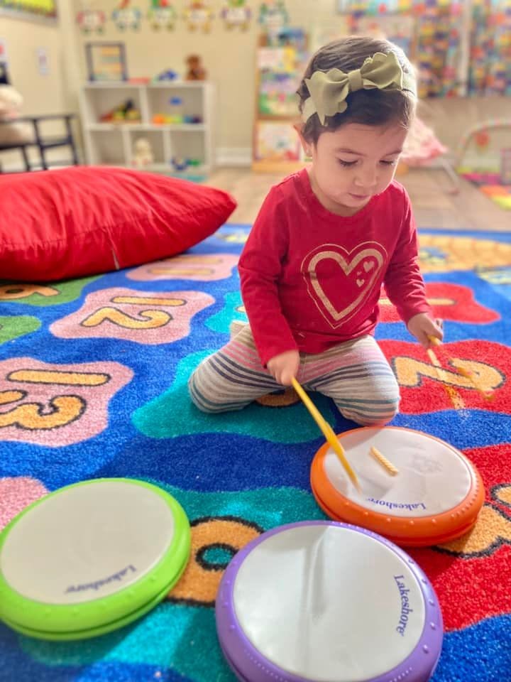 Child playing with toy drums on a colorful rug