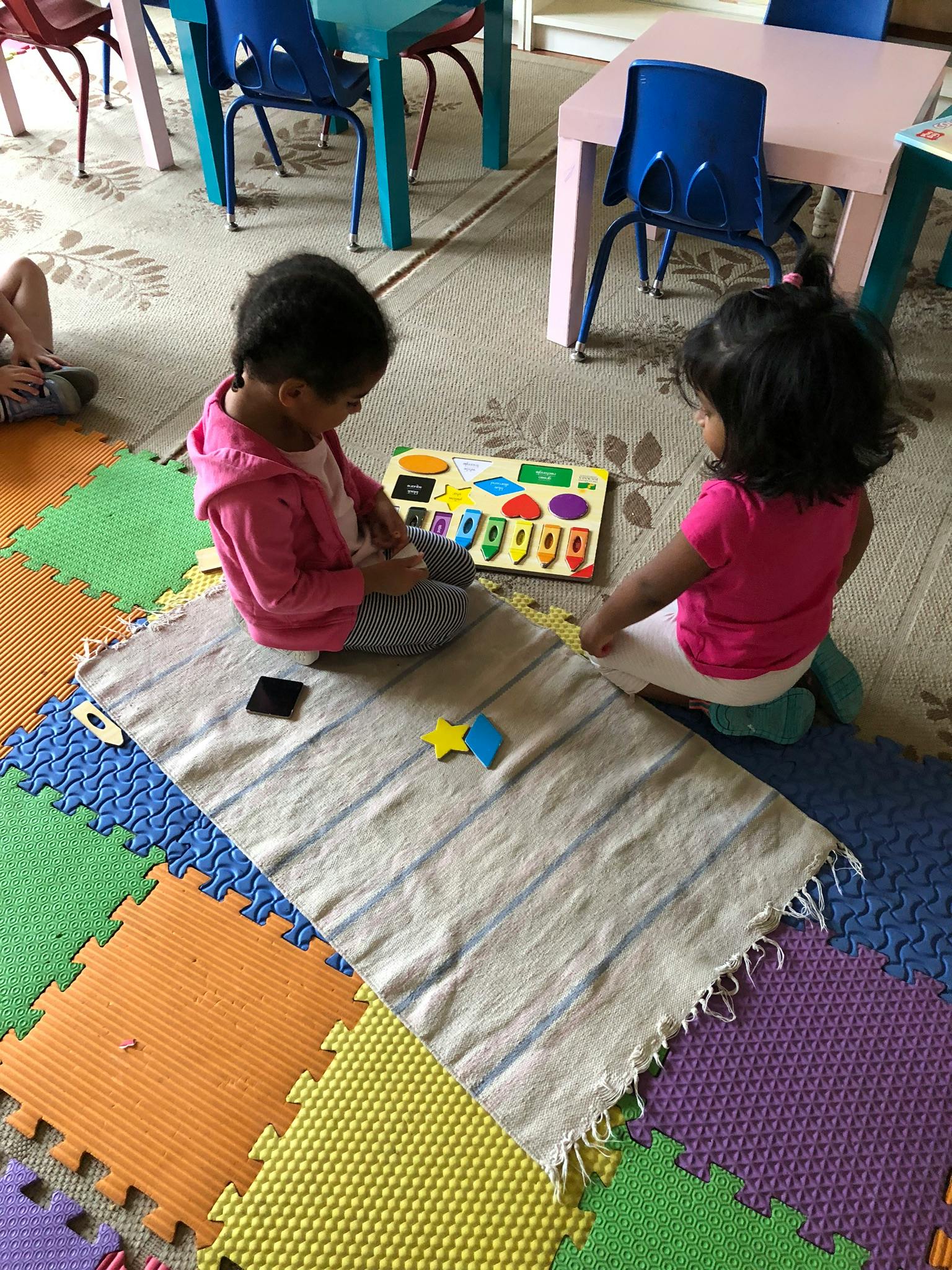 Two children playing with a shape sorter puzzle on a rug