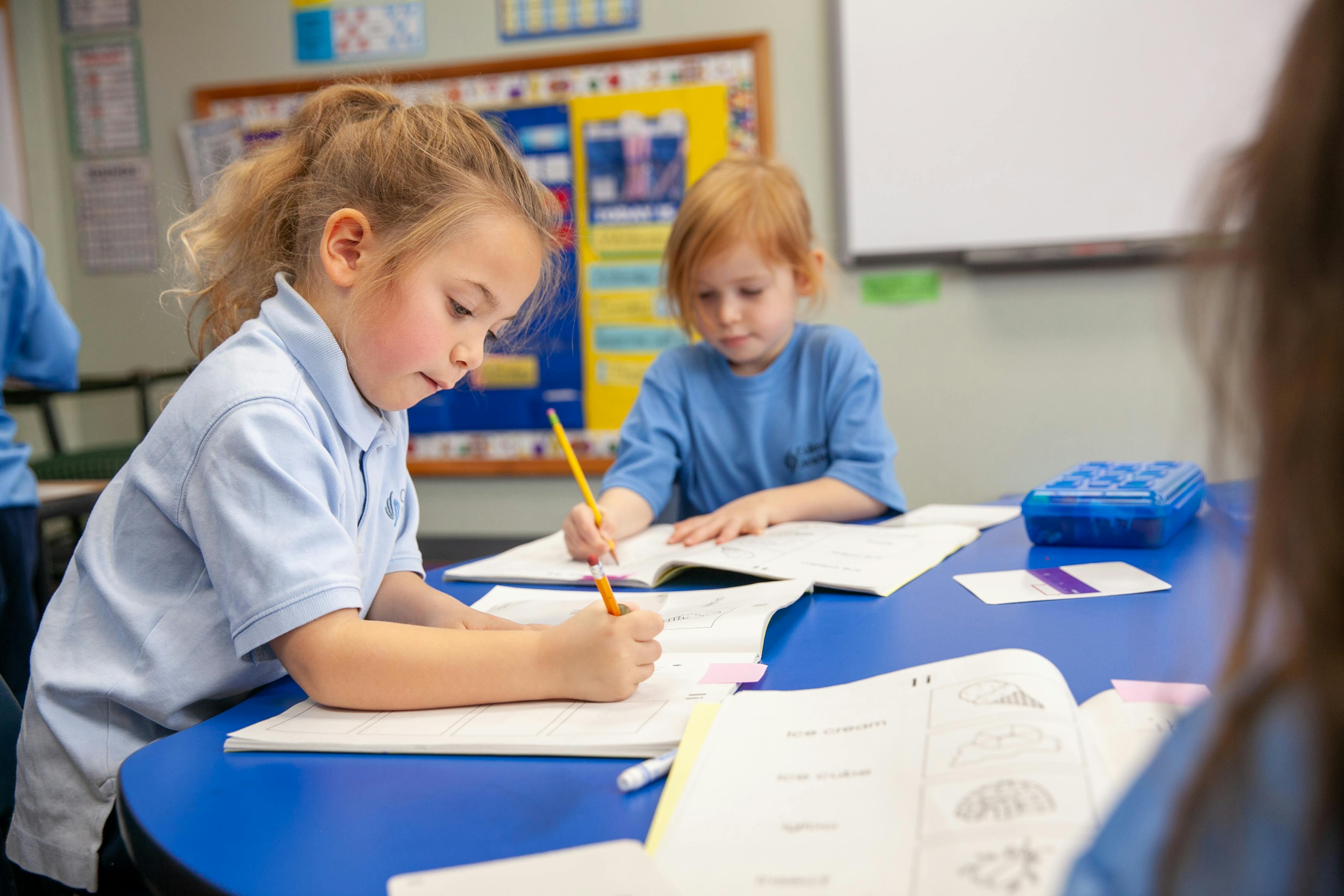 Two children writing at a table in a classroom