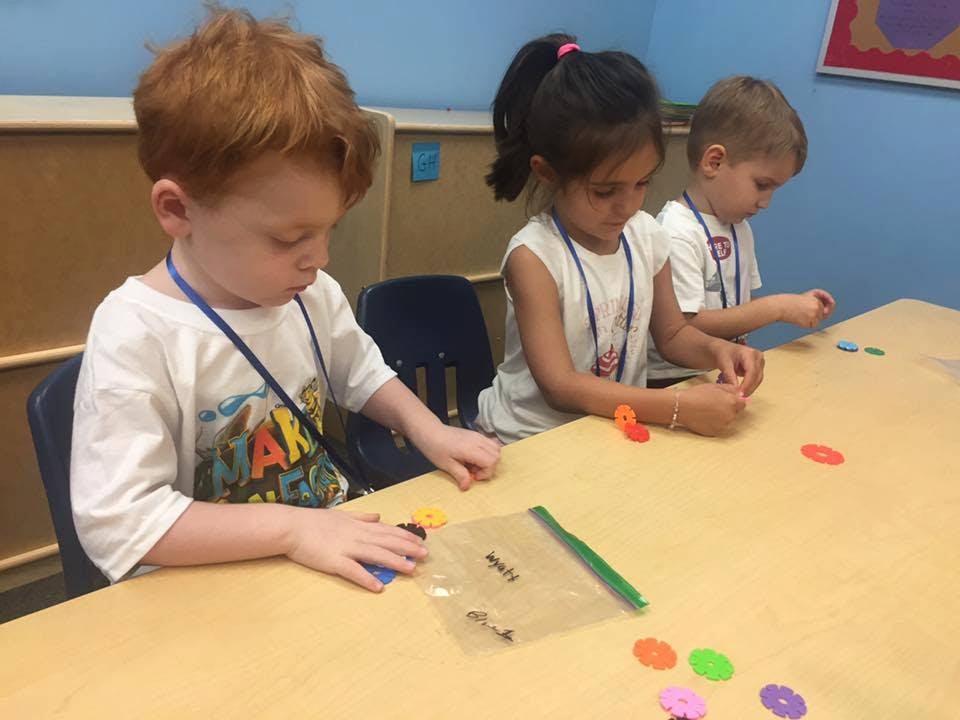 Three children sitting at a table, engaged in an activity with small objects