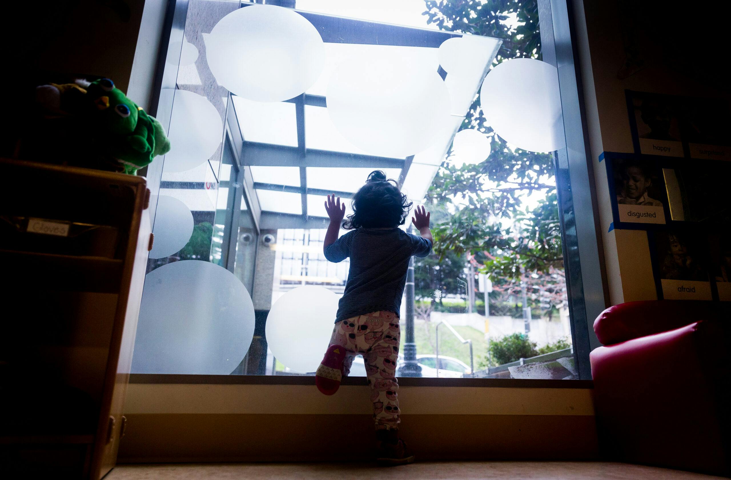 Child looking out a large window, hands pressed against the glass