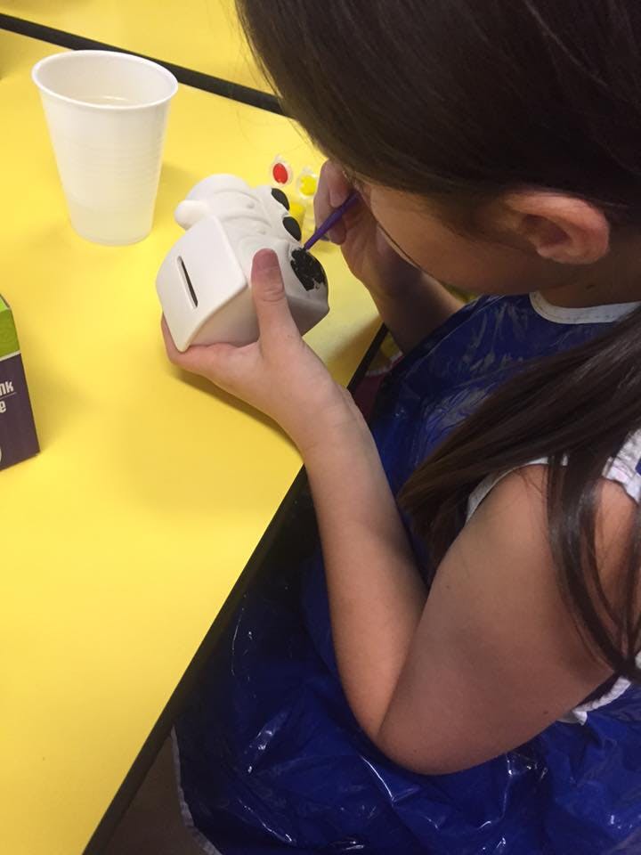Child painting a ceramic object with a small brush