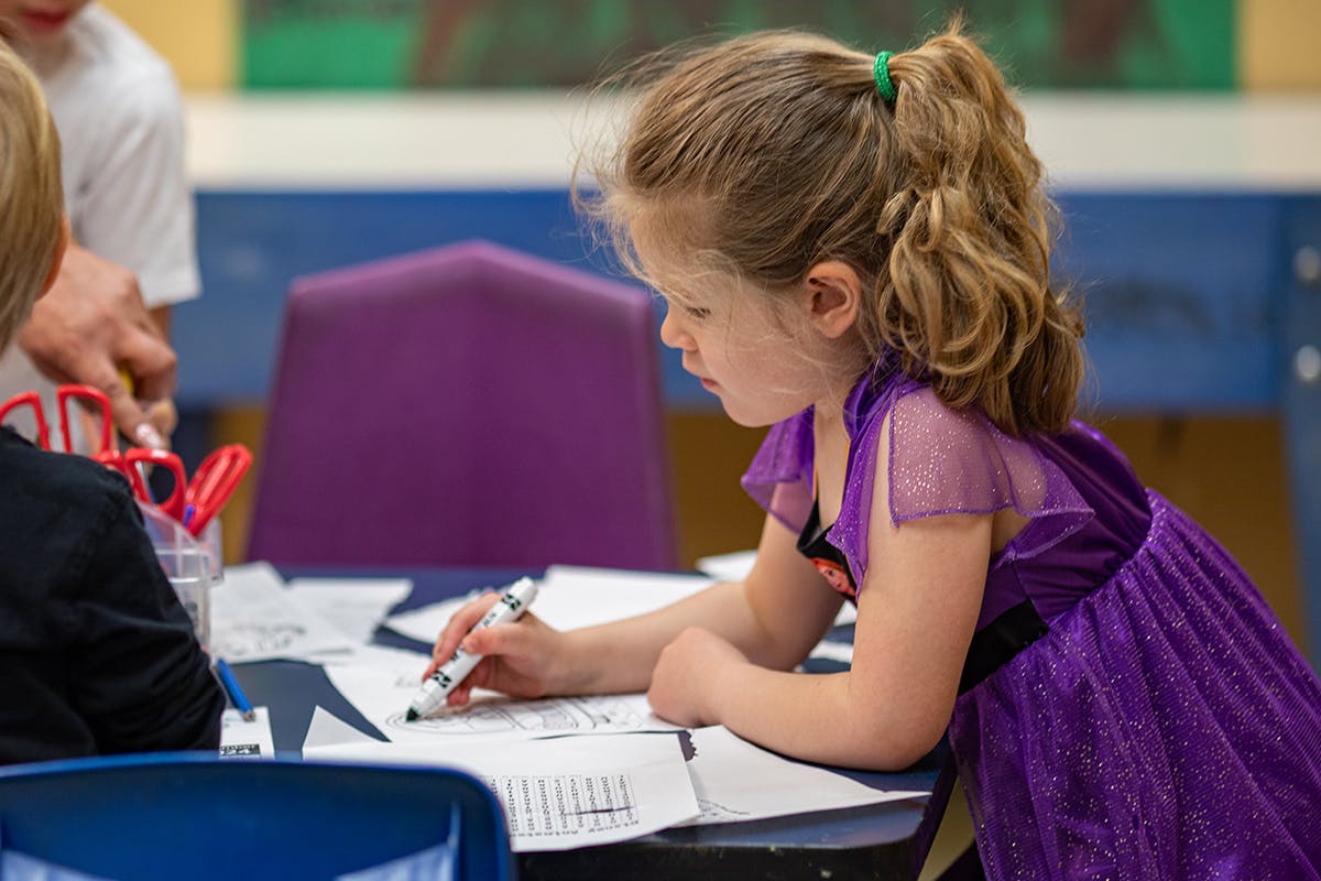 Child in purple dress writing on paper at a table