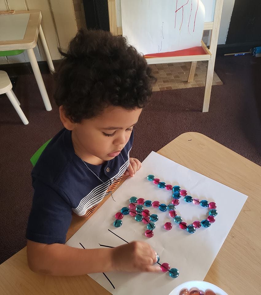Child arranging colorful beads on a paper with lines