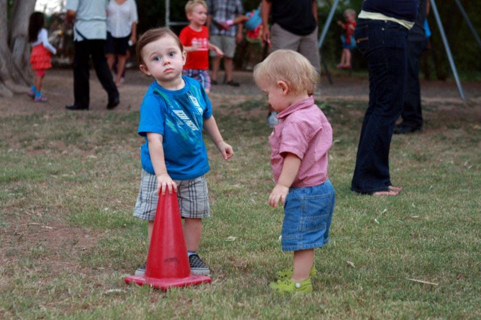 Two children standing on grass, one holding a red cone