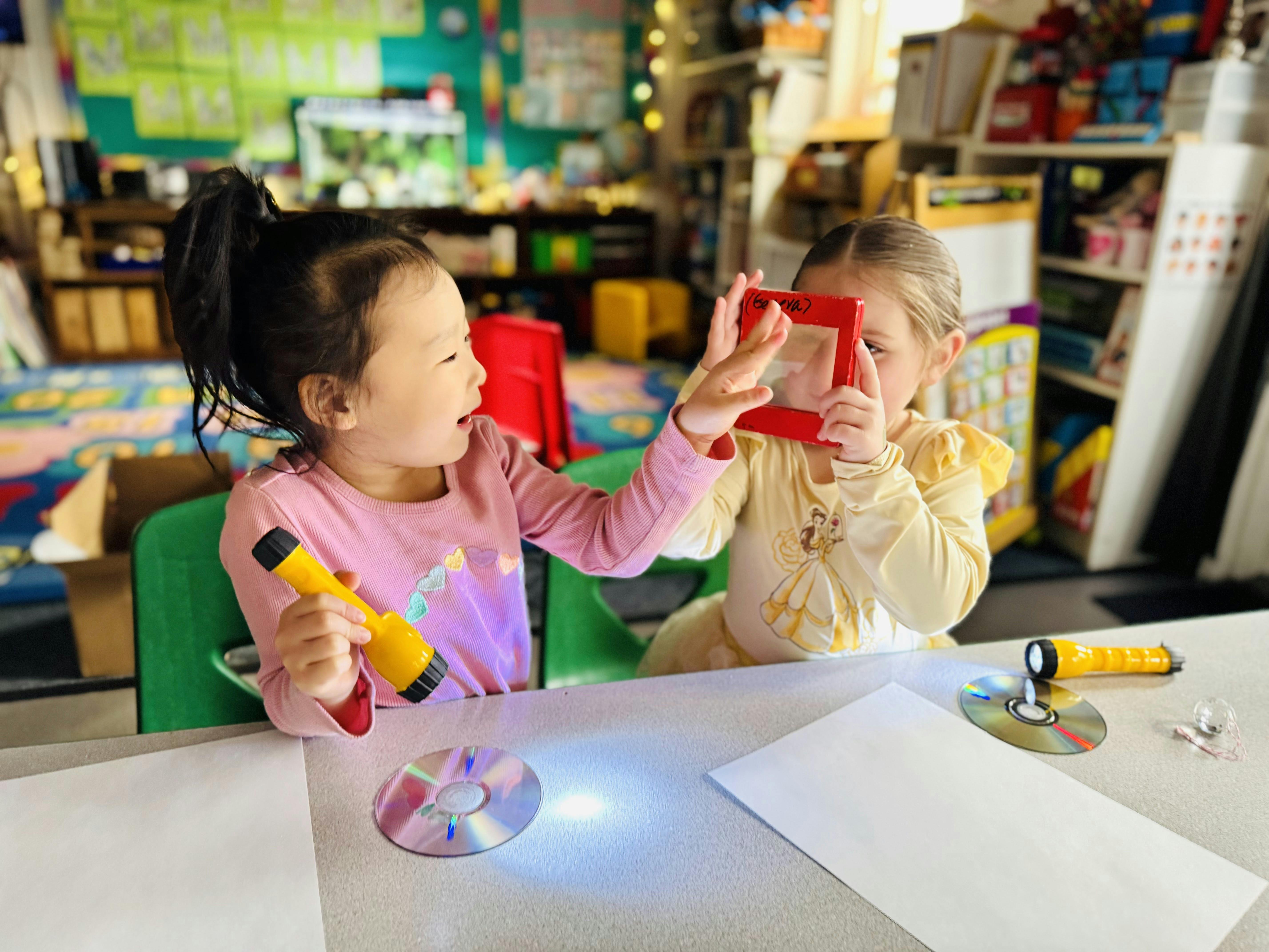 Two children at a table, one holding a flashlight, the other holding a red viewer