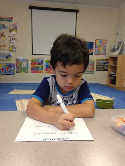 Child writing on paper at a desk in a classroom