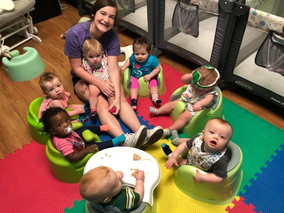 Person sitting on floor surrounded by multiple babies in chairs