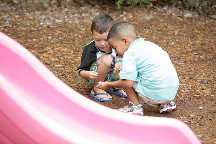 Two children crouching and looking at something on the ground