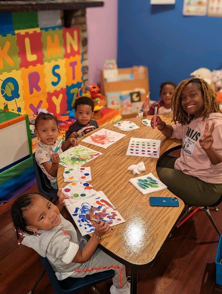 Adult and children painting at a table in a classroom
