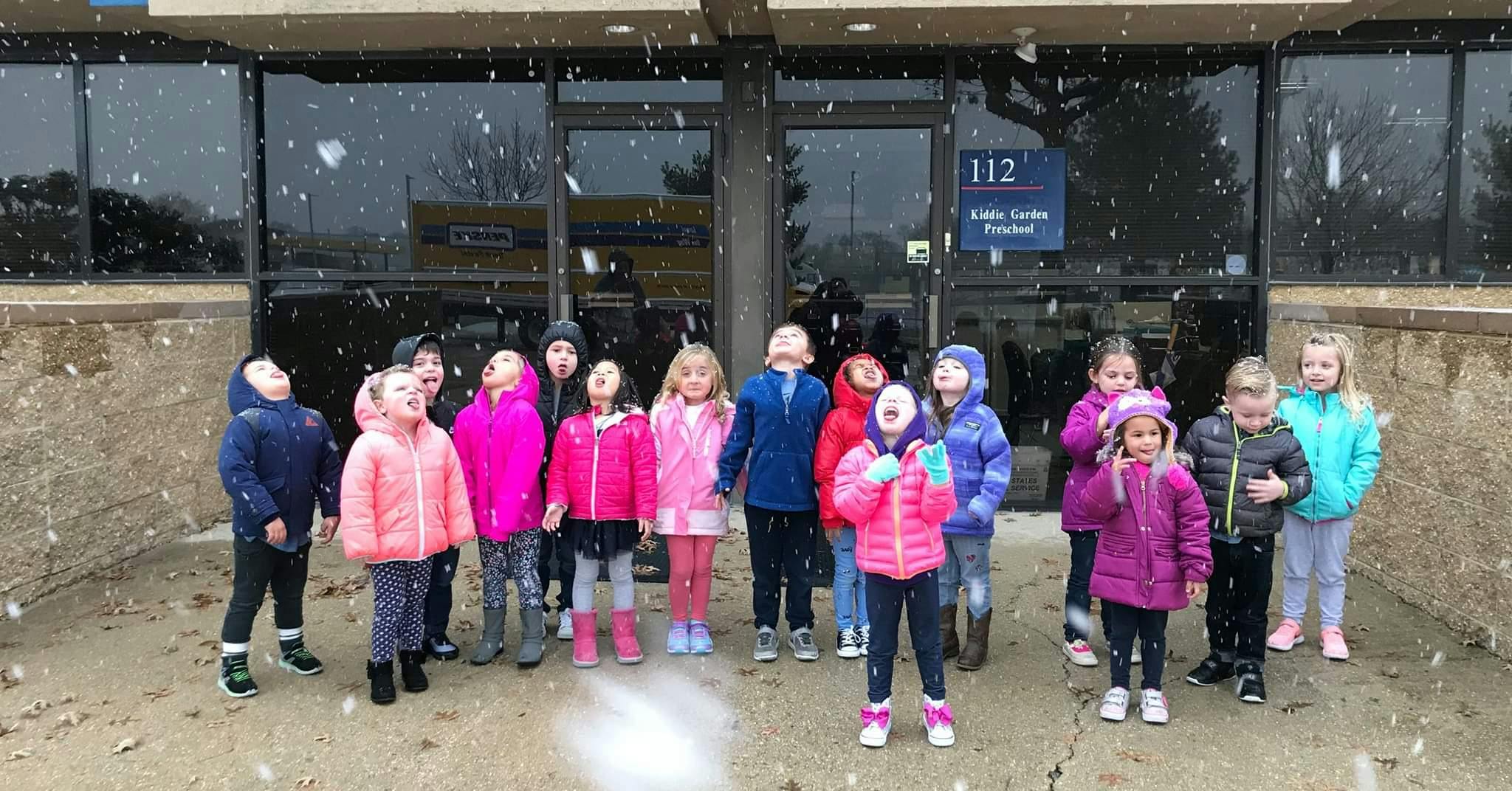 Group of children looking up at falling snow outside a building