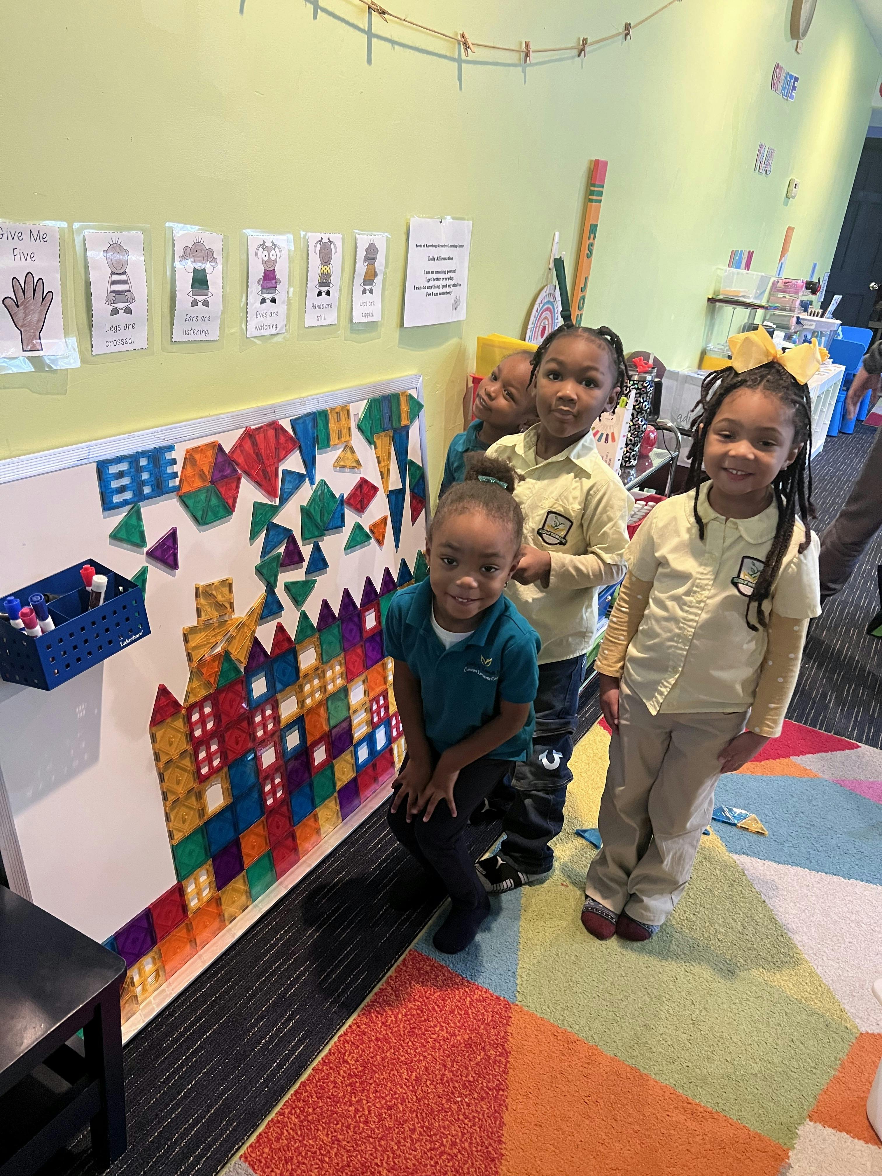 Four children standing next to a whiteboard covered in colorful magnetic shapes