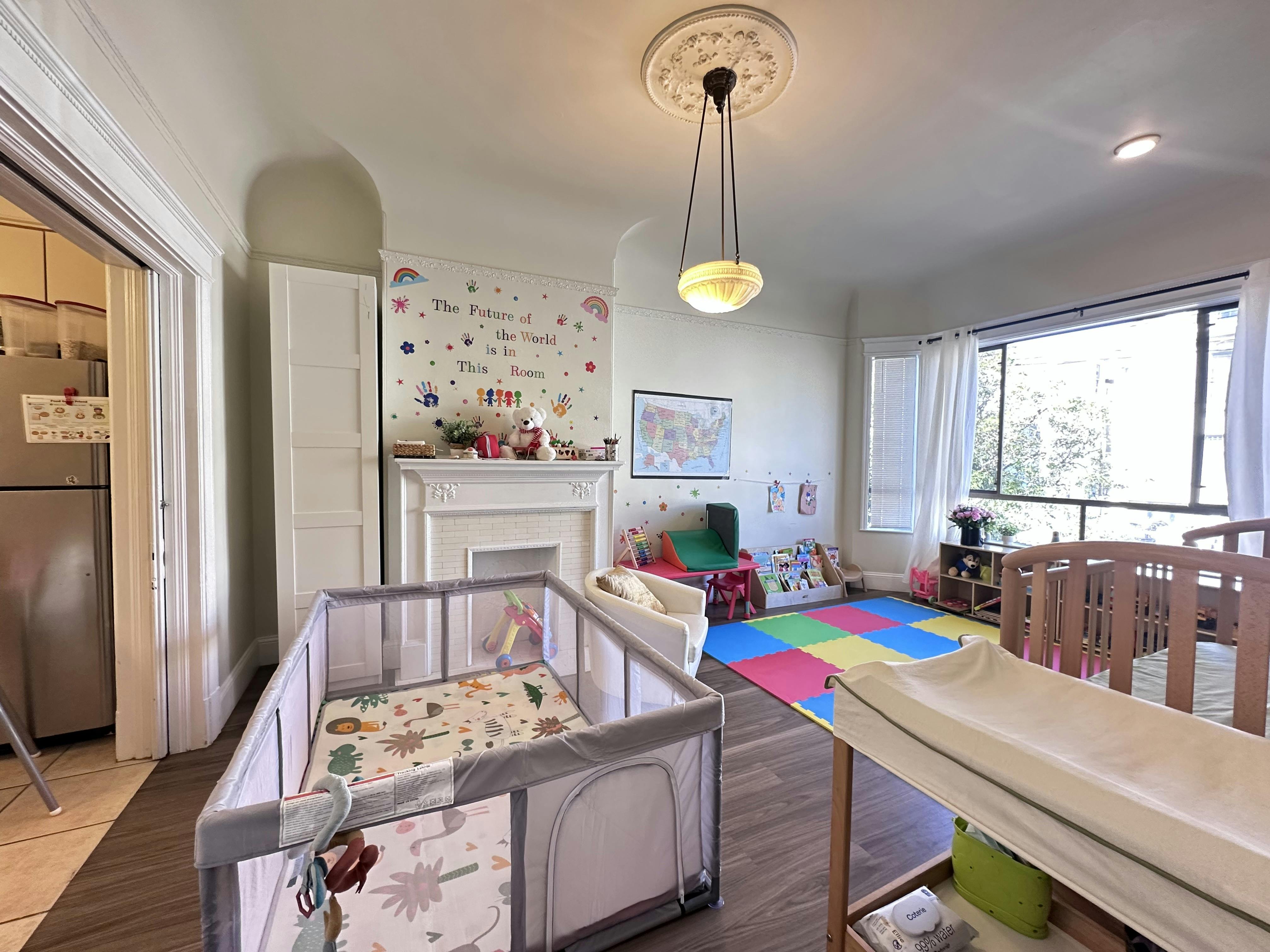 a brightly lit daycare room with playpens, a changing table, and a mural that says 'The Future of the World is in This Room'