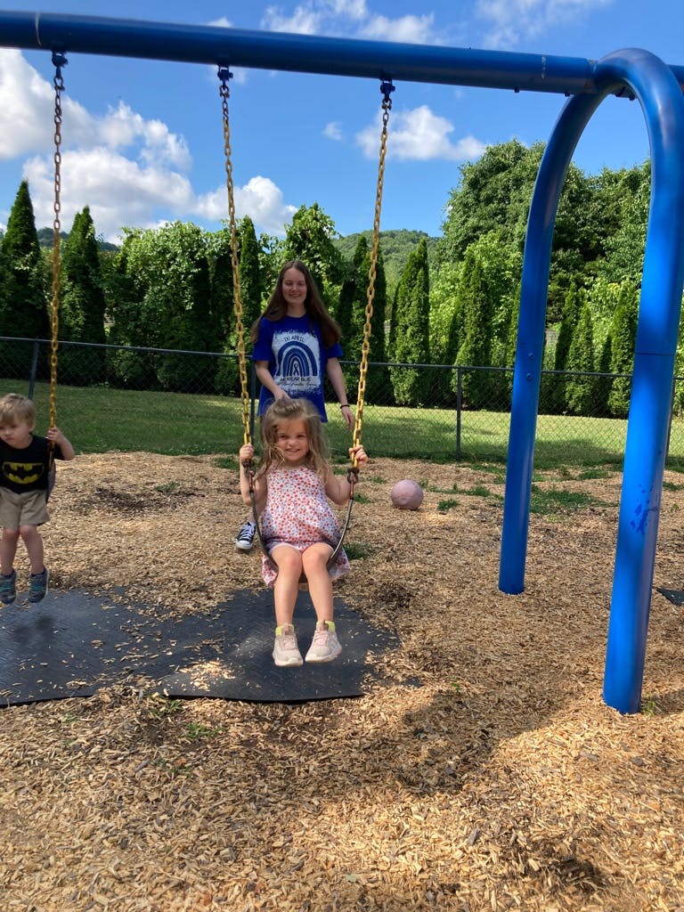 Person pushing a child on a swing, another child on a swing nearby