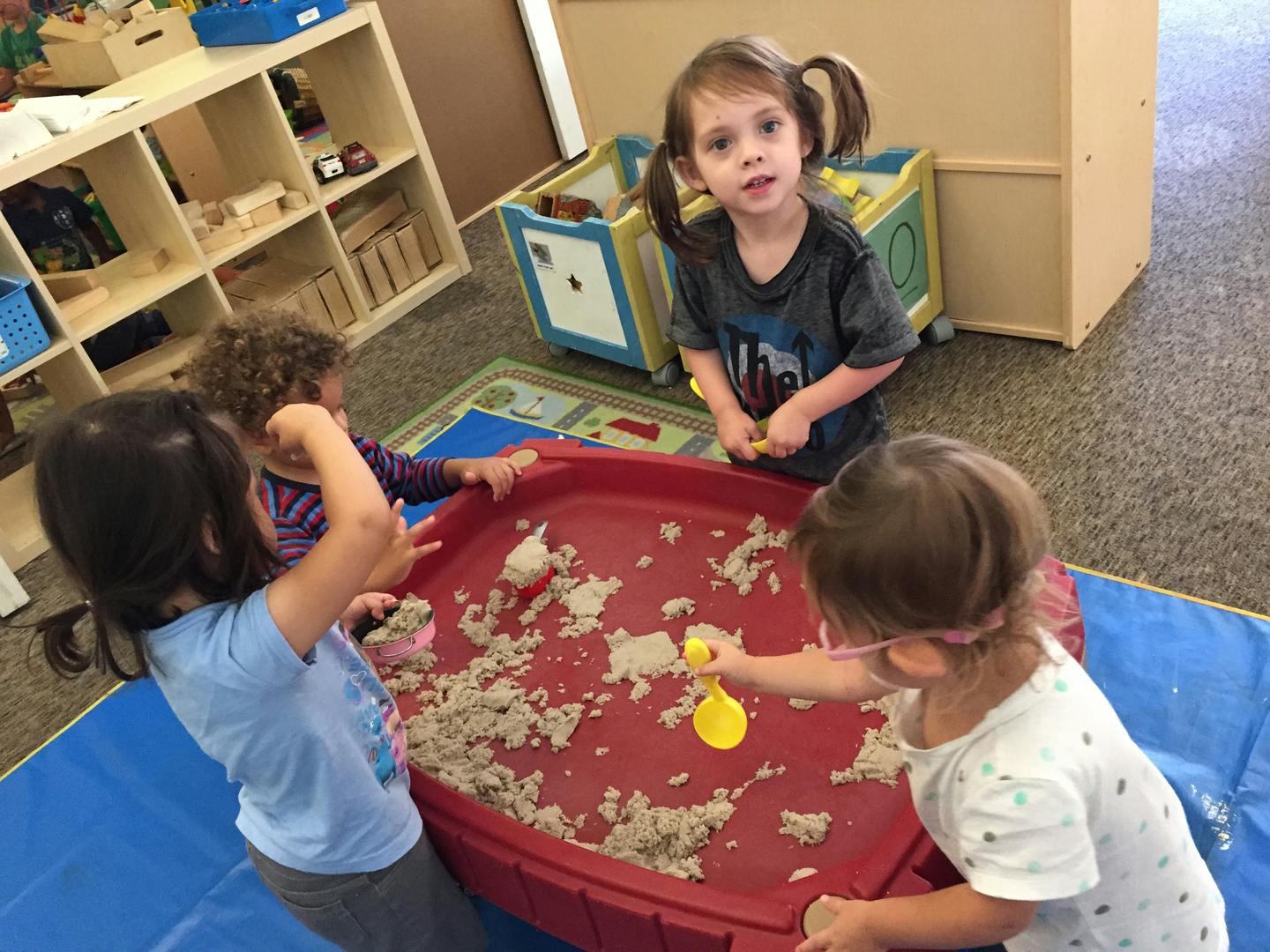 Children playing with sand in a red bin