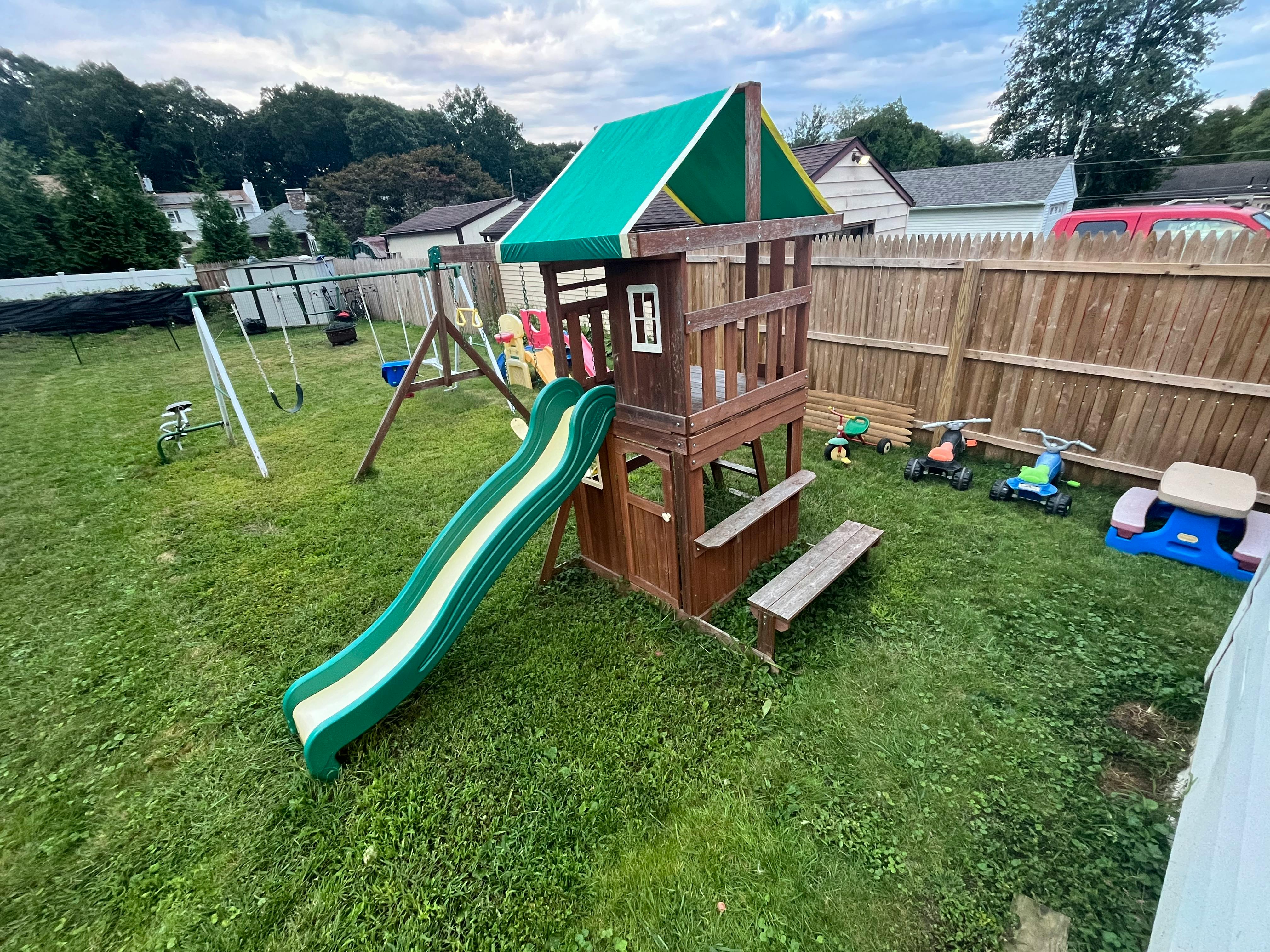 Playground with a wooden playhouse, green slide, and swings in a grassy yard