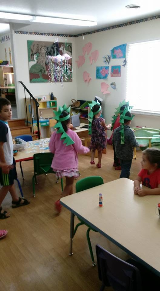 Children in a classroom, some wearing green headpieces