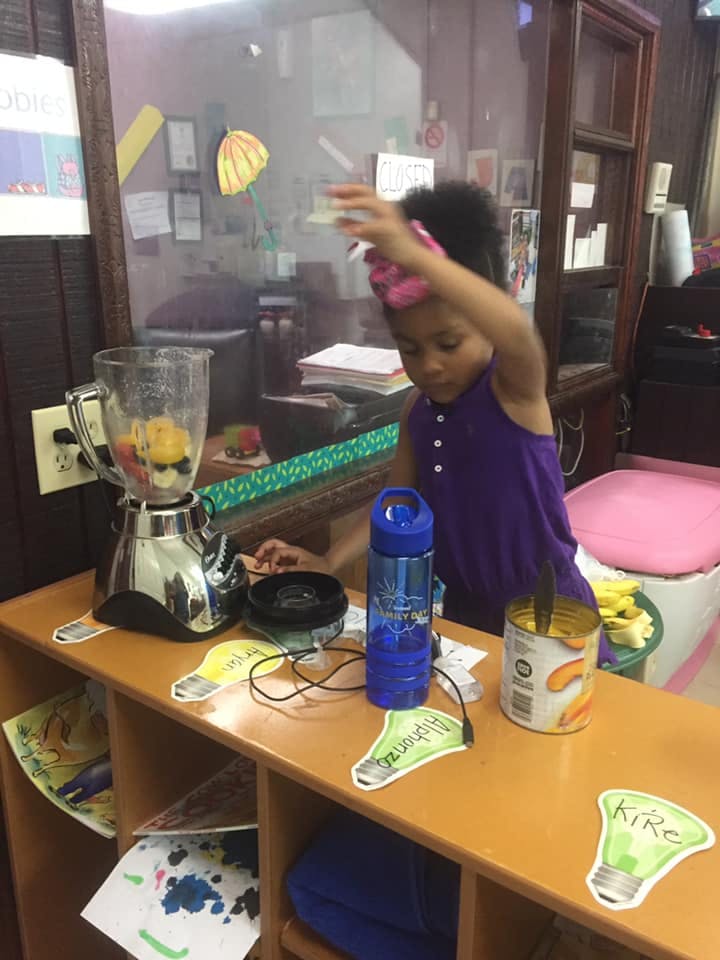 Child standing at a counter with a blender filled with fruit