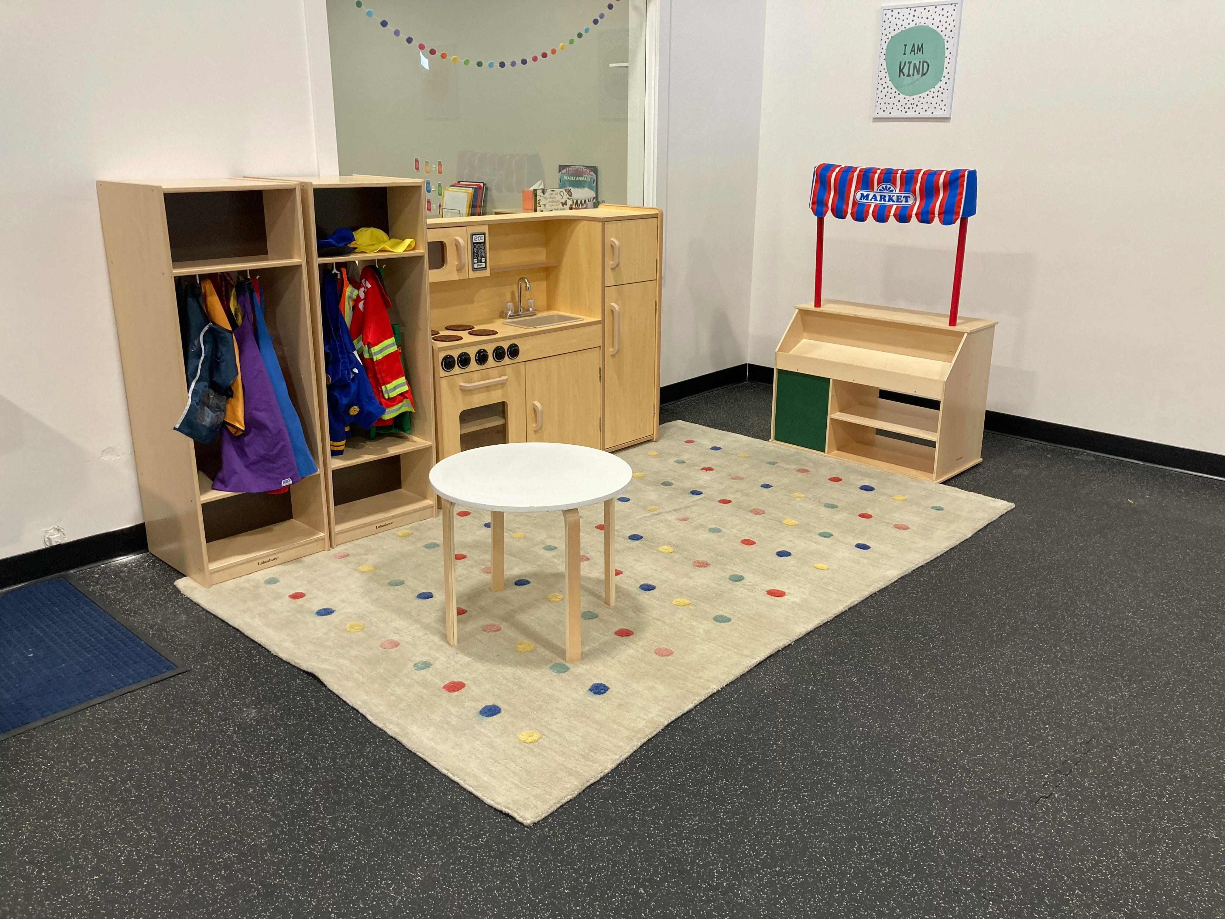 Playroom with a small table, rug, play kitchen, and dress-up clothes