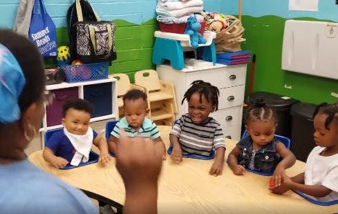Adult interacting with four young children at a table in a classroom