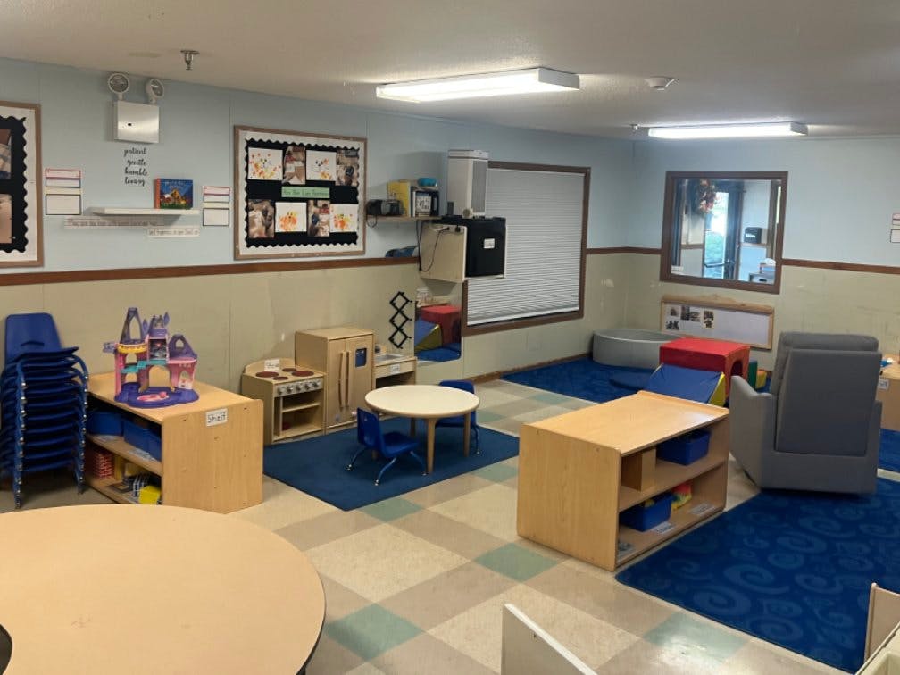 A colorful classroom with play kitchen, small tables, and blue rugs