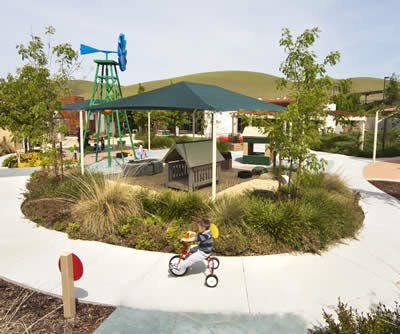 Child on a tricycle on a path next to a playground