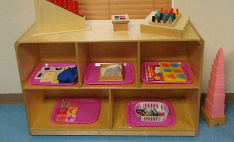 Wooden shelf with pink trays holding various learning materials